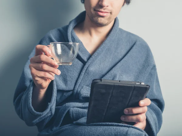 Человек в халате с пустой чашкой с помощью планшета — стоковое фото