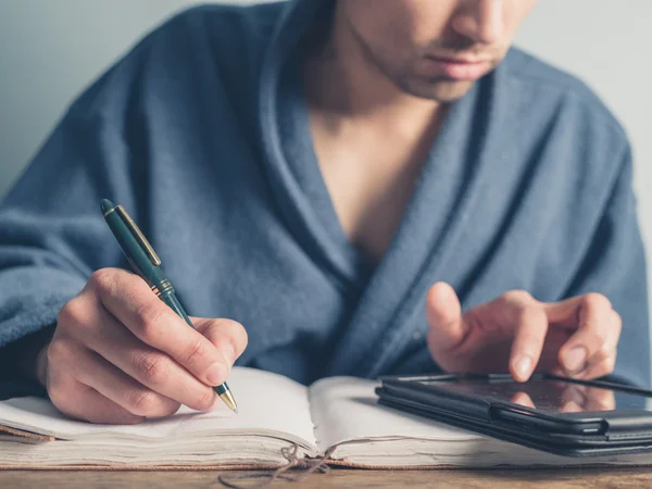 Hombre en albornoz usando mesa y tomando notas —  Fotos de Stock