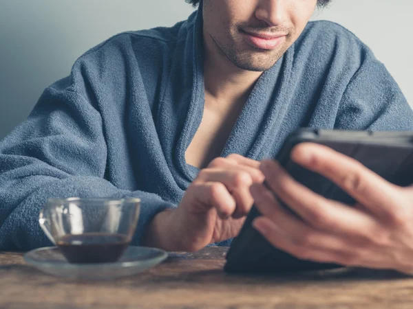 Mann im Bademantel trinkt Kaffee und benutzt Tablette — Stockfoto