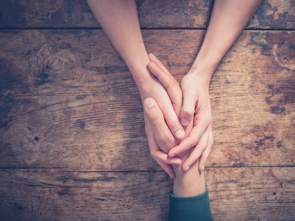 Hombre y mujer tomados de la mano en una mesa — Foto de Stock