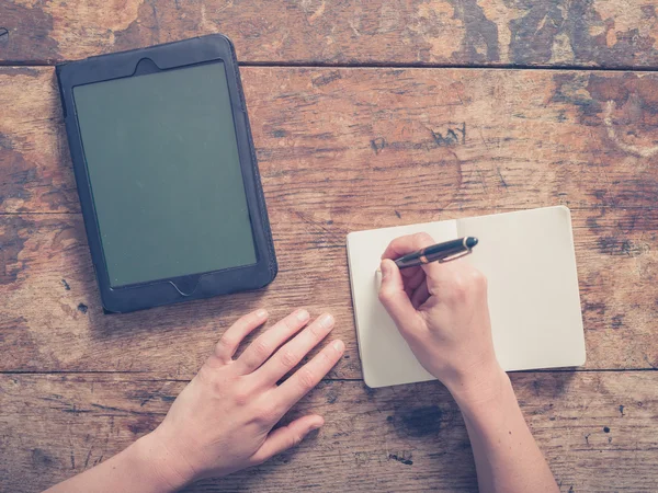 Woman writing in notepad and using tablet — Stock Photo, Image