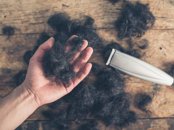 Рука держа волосы и ножницы
