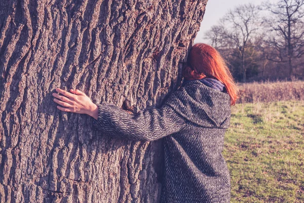 年轻女子在冬季中拥抱一棵大树 — 图库照片
