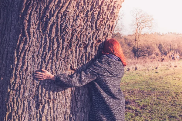 Młoda kobieta przytulanie wielkie drzewo w zimie — Zdjęcie stockowe