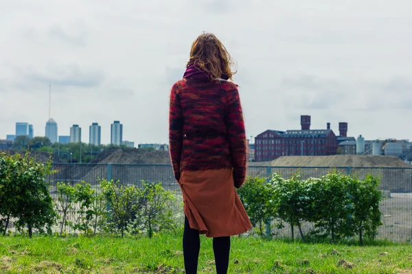Молодая женщина, стоящая на траве и любующаяся городом — стоковое фото