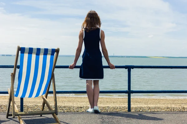 Mulher admirando o mar do passeio com uma cadeira de praia — Fotografia de Stock