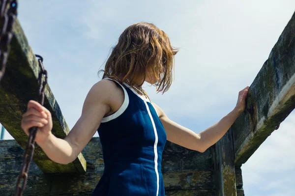 Young woman in blue dress standing by wooden beams — Stock Photo, Image