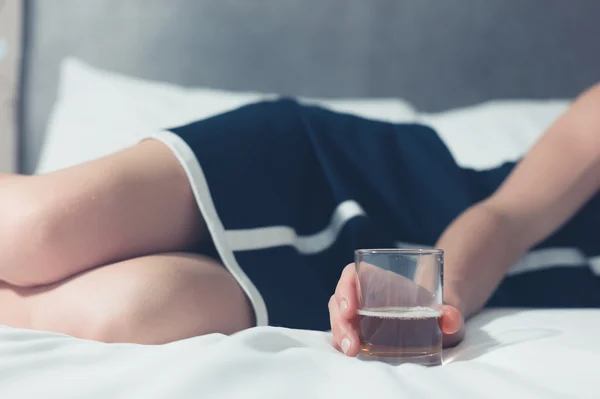 Mujer joven acostada en la cama con vidrio en la mano — Foto de Stock