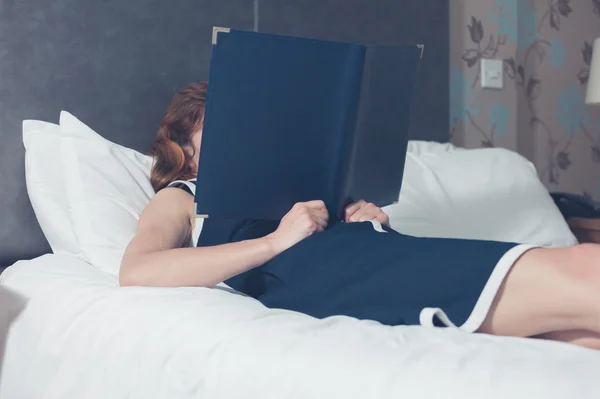 Woman lying on bed in hotel room reading — Stock Photo, Image