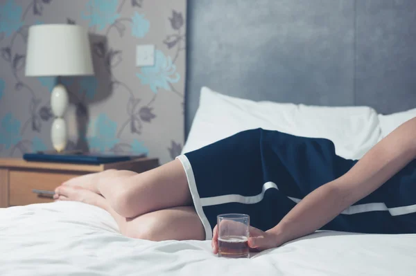 Mujer joven acostada en la cama con vidrio en la mano — Foto de Stock