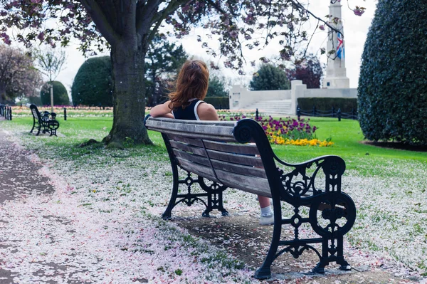 Элегантная женщина на скамейке в парке с цветущей вишней — стоковое фото