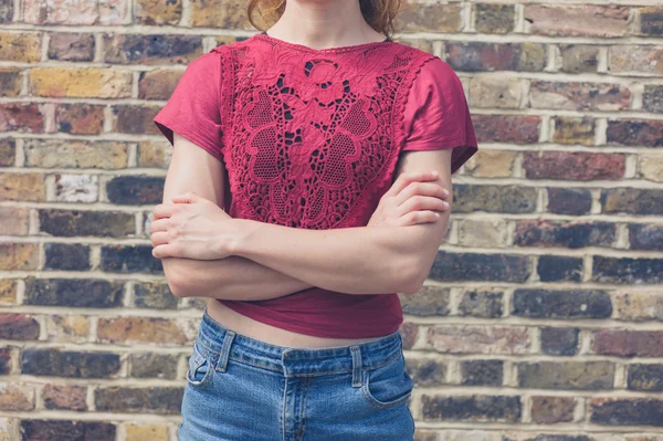 Young woman in red top standing by brick wall — Stock Photo, Image