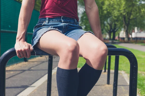 Jonge vrouw zitten op een rail in park — Stockfoto