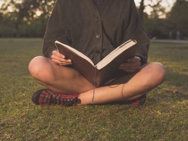 Gün batımında parkta kitap okuyan genç bir kadın.
