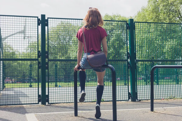 Giovane donna seduta su una rotaia nel parco — Foto Stock