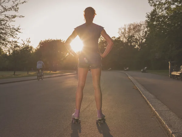 Mladá žena nosí kolečkové brusle v parku při západu slunce — Stock fotografie