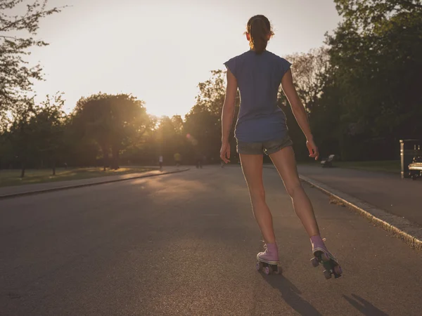 Jonge vrouw rolschaatsen in park bij zonsondergang — Stockfoto