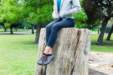 Park ağaç gövdesi üzerinde oturan genç kadın