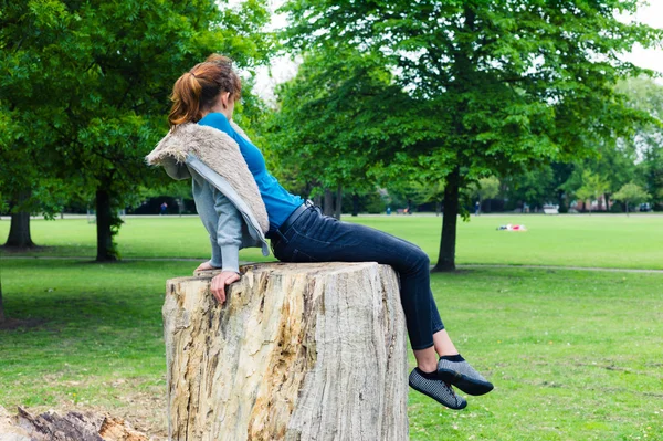 Ung kvinna sitter på trädstam i park — Stockfoto