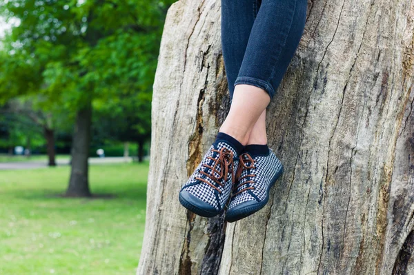 Benen van jonge vrouw zittend op de boomstam — Stockfoto