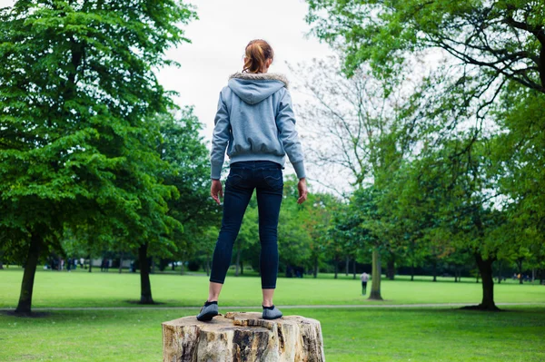 Jonge vrouw staande op een boomstam in park — Stockfoto