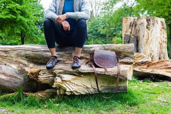 Woman sitting on tree trunk with a handbag — Stock Photo, Image