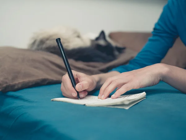 Kvinnan tar anteckningar i sängen med katten — Stockfoto