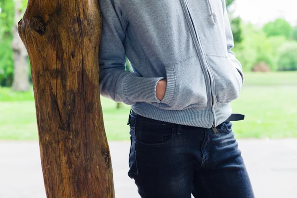 Woman leaning against wooden post in park — Stock Photo, Image