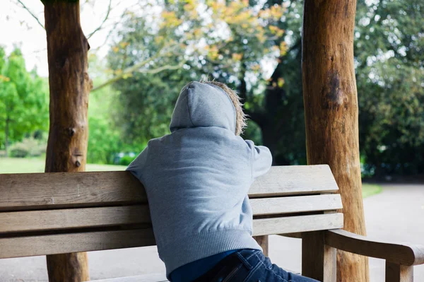 Persona con cappuccio seduta sulla panchina del parco — Foto Stock