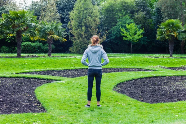 Mujer de pie junto a macizos de flores en el parque —  Fotos de Stock