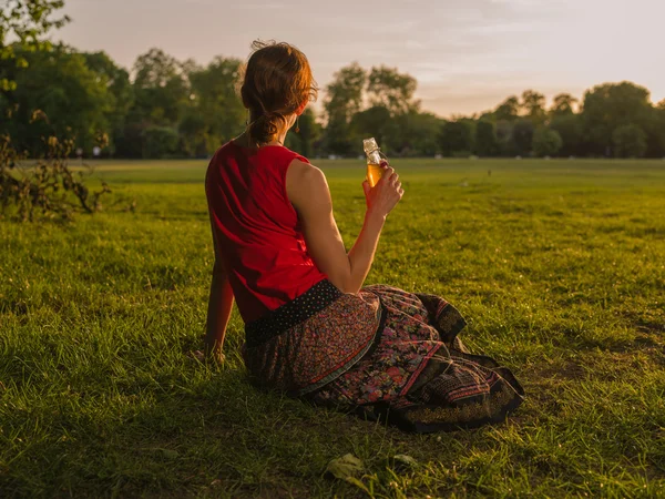 Mulher bebendo e admirando o pôr do sol no parque — Fotografia de Stock