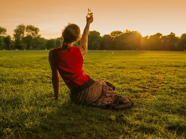 Žena, zvedání láhev na západ slunce v parku — Stock fotografie