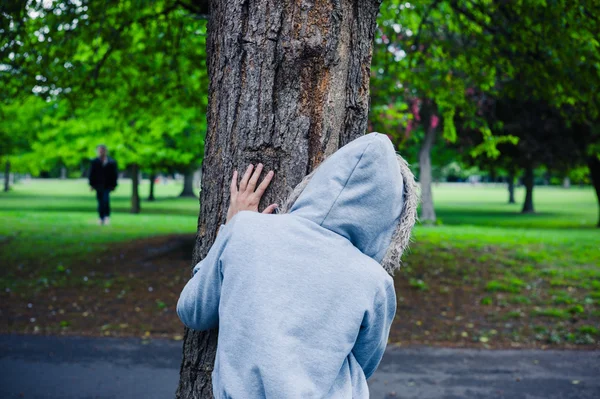 Persona incappucciata nascosta dietro un albero — Foto Stock