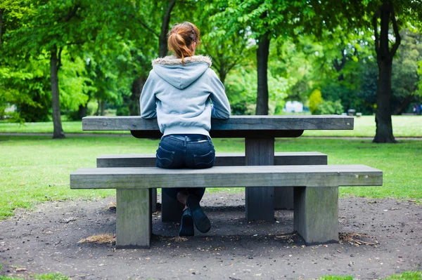 Jovem mulher sentada em banco por mesa no parque — Fotografia de Stock