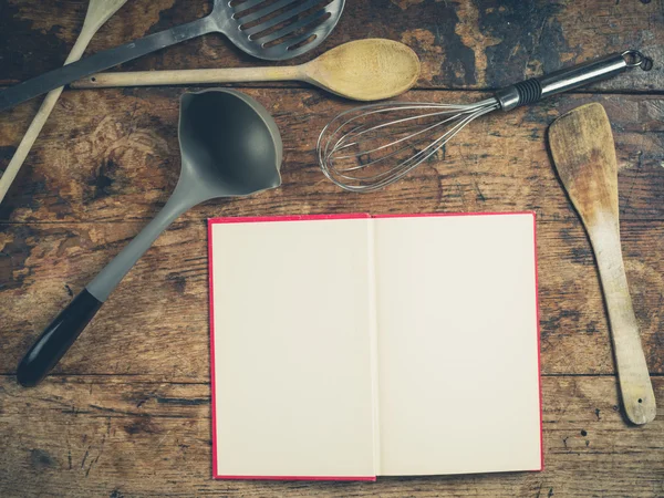 Utensílios de cozinha em mesa de madeira com livro — Fotografia de Stock