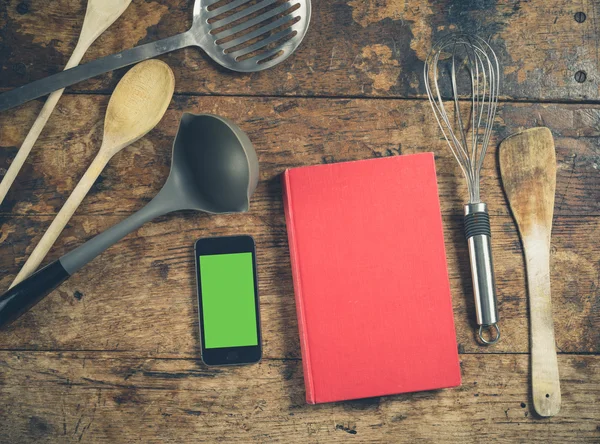Utensílios de cozinha em mesa de madeira com livro e telefone inteligente — Fotografia de Stock