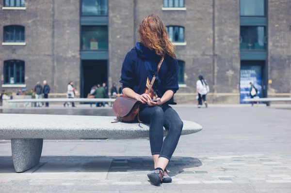 Mujer sentada en un banco de granito usando un teléfono inteligente — Foto de Stock