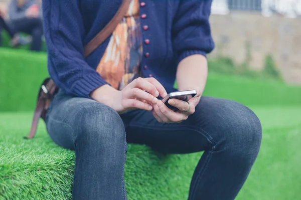 Akıllı telefon kullanarak astro çim üzerinde oturan kadın — Stok fotoğraf