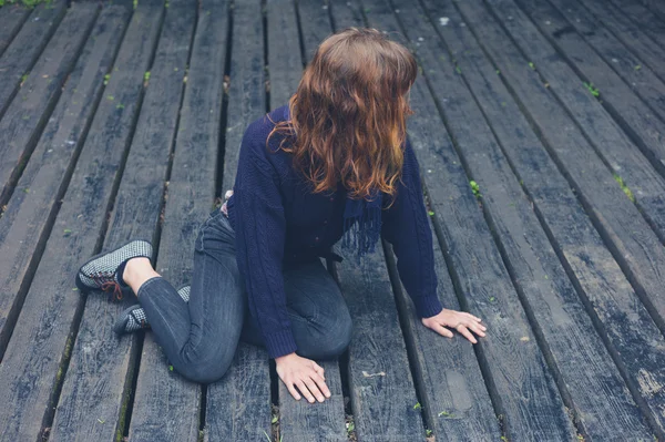 Молодая женщина сидит на деревянной палубе — стоковое фото