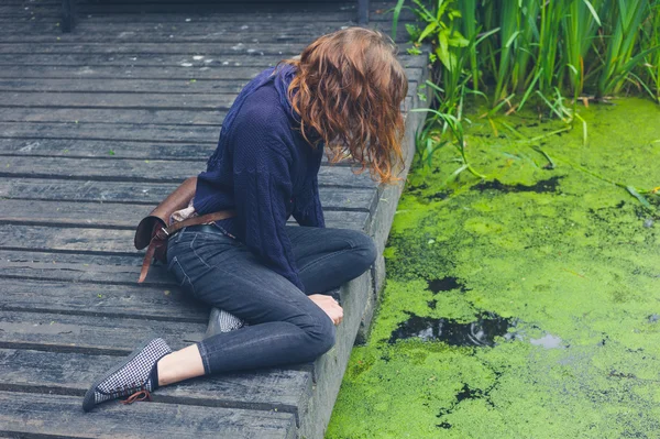 Vrouw zitten op het houten dek door vijver — Stockfoto