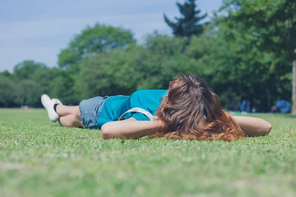 Genç bir kadın parkta çimlerin üzerinde yatıyor. — Stok fotoğraf