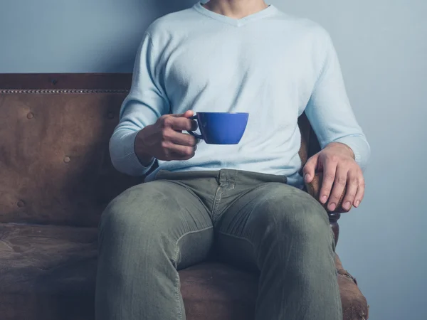 Человек на диване пьет кофе — стоковое фото