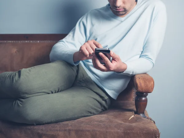 Mladý muž sedí na pohovce a pomocí smartphonu — Stock fotografie