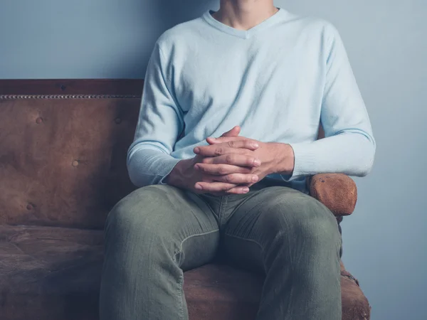 Jeune homme assis sur un canapé avec les mains pliées — Photo