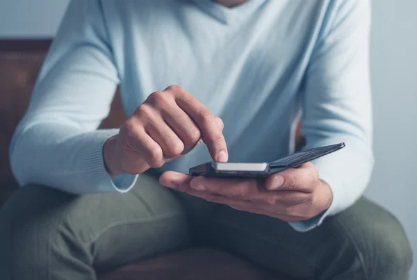 Junger Mann sitzt auf Sofa und benutzt Smartphone — Stockfoto