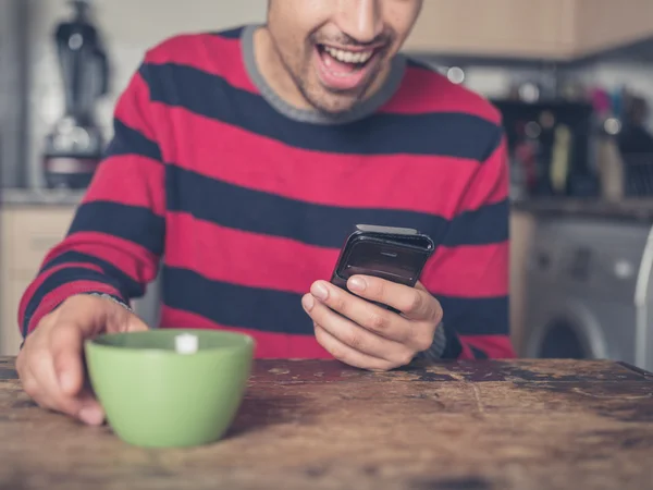 Glücklicher junger Mann benutzt Smartphone in Küche — Stockfoto