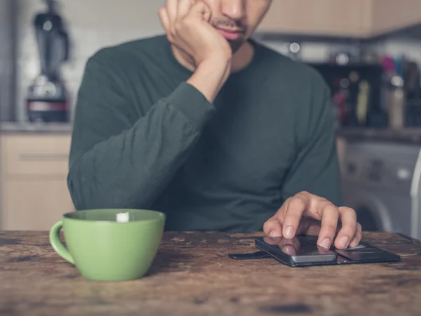 Hombre joven bebiendo café y usando el teléfono inteligente — Foto de Stock