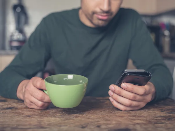 Junger Mann trinkt Kaffee und benutzt Smartphone — Stockfoto