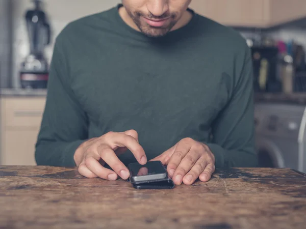 Junger Mann benutzt Smartphone in Küche — Stockfoto