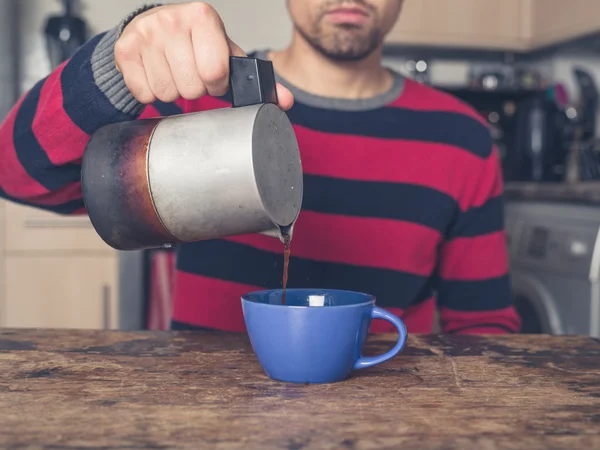 Junger Mann gießt Kaffee in Küche ein — Stockfoto